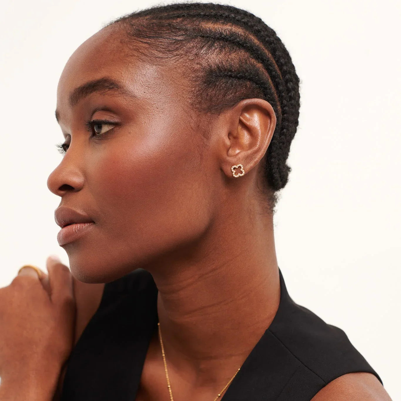 Close-up profile of woman with braided hair wearing gold clover stud earrings and black top
