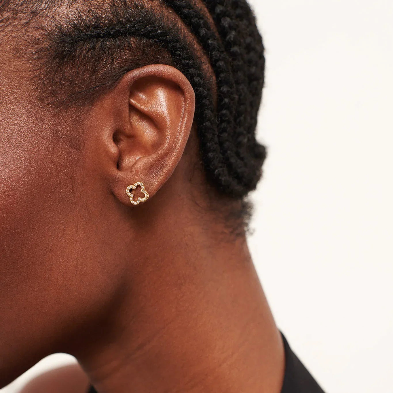 Close-up of woman with braided hair wearing small gold clover-shaped stud earrings with diamonds