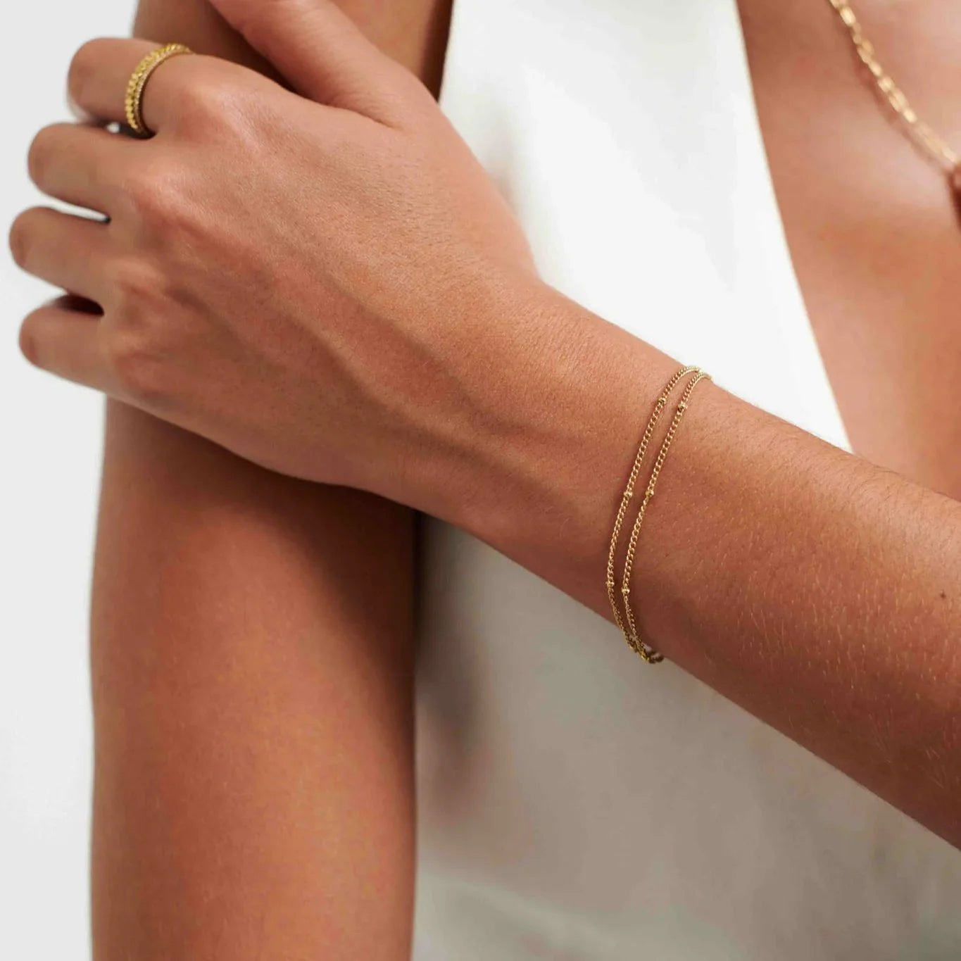 Close-up of woman's arm wearing delicate double-strand gold bracelet and matching gold ring