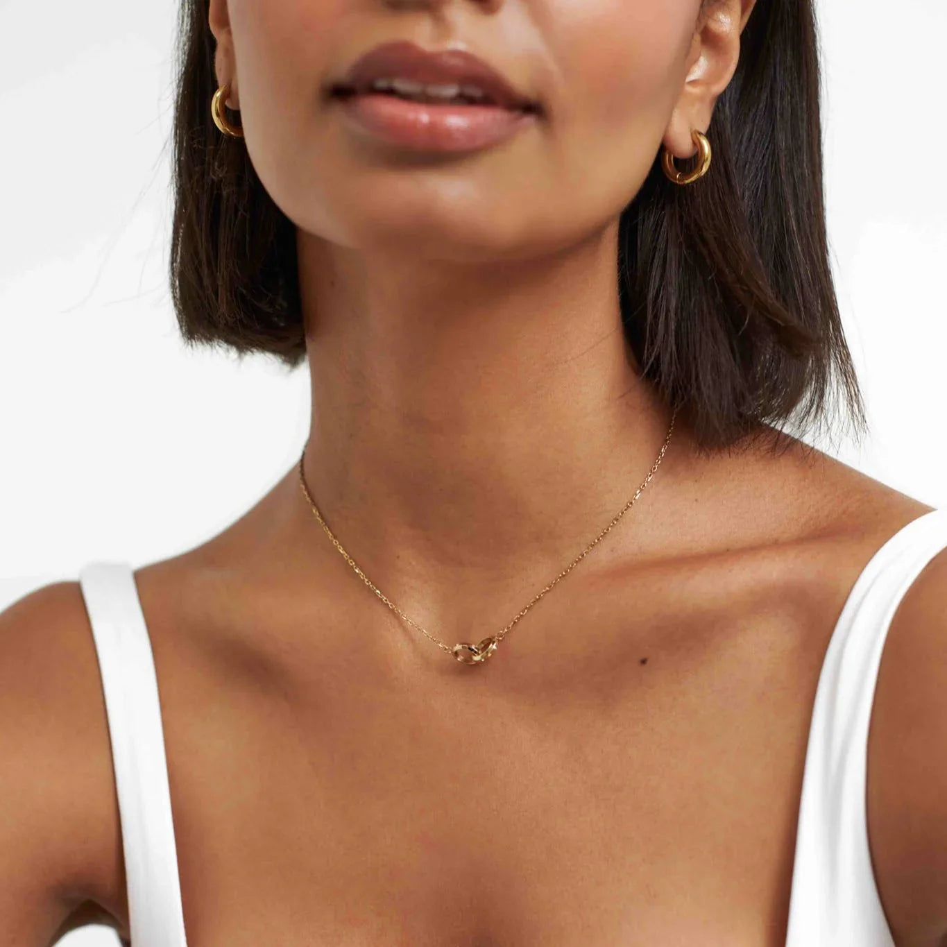 Close-up of woman wearing gold hoop earrings and a delicate gold chain necklace with interlocking links