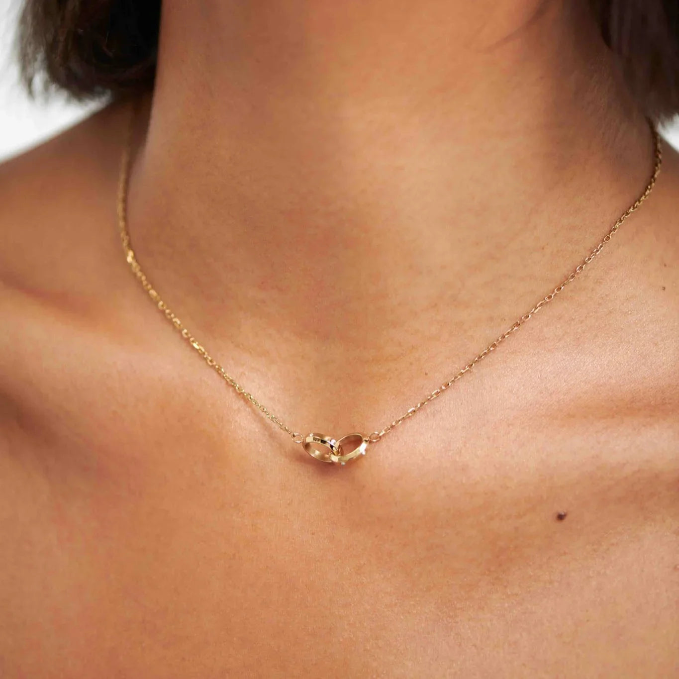Close-up of woman wearing delicate gold chain necklace with two interlocking rings pendant