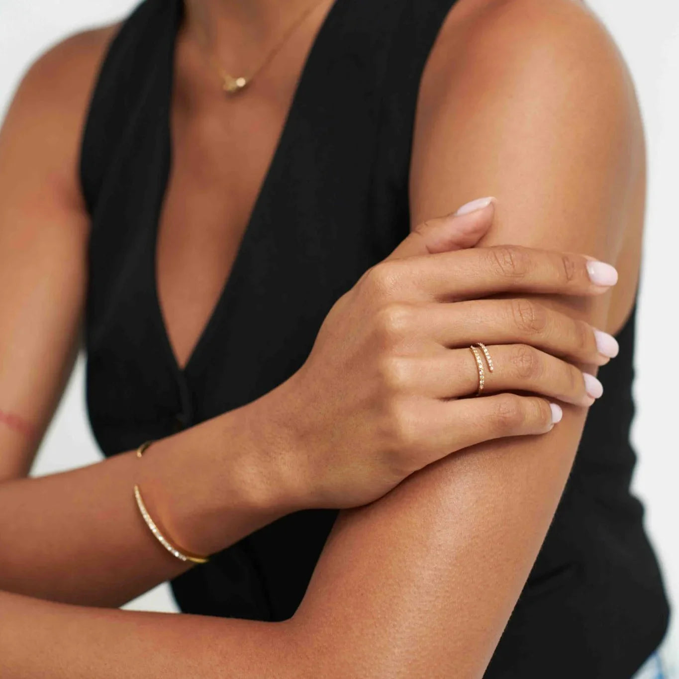 Close-up of woman wearing gold bracelet, diamond ring, and black sleeveless top