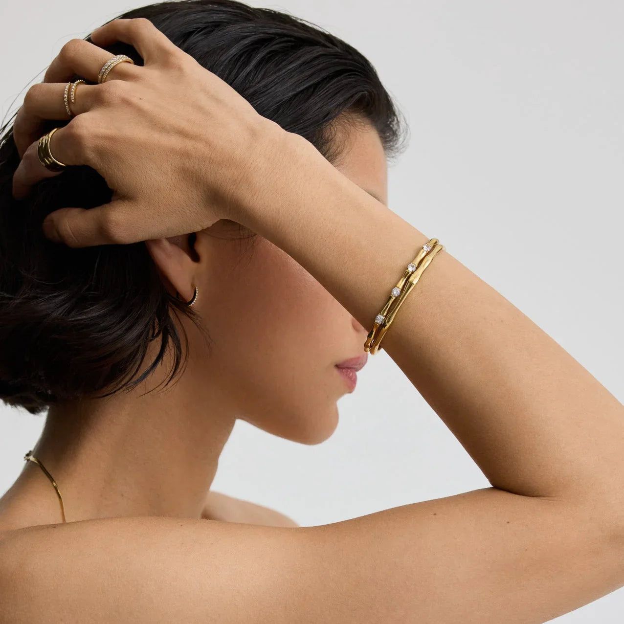 Close-up of woman wearing gold bamboo-style bracelets with diamonds and gold rings on fingers