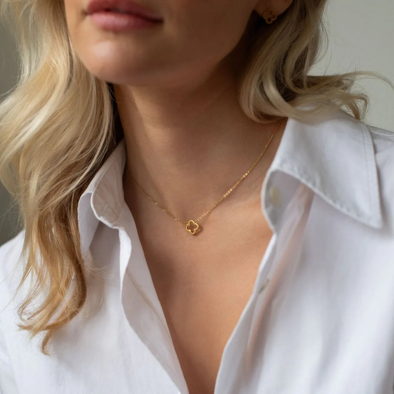 Close-up of woman wearing gold clover pendant necklace and white shirt with blonde hair detail