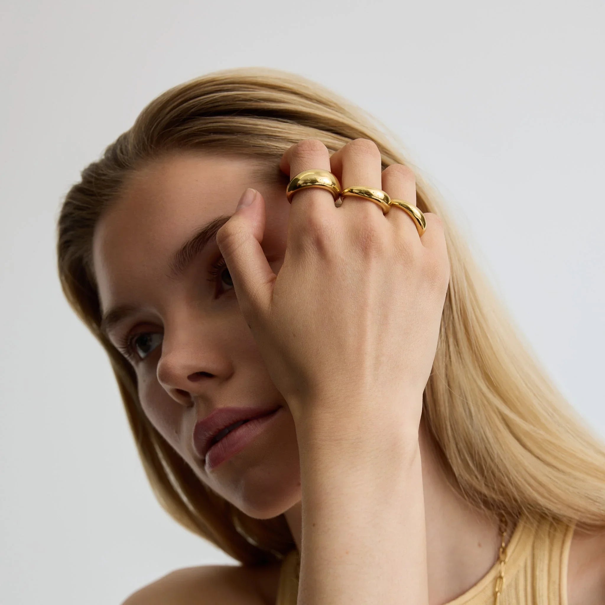 Close-up of woman wearing three shiny gold dome rings on fingers against neutral background