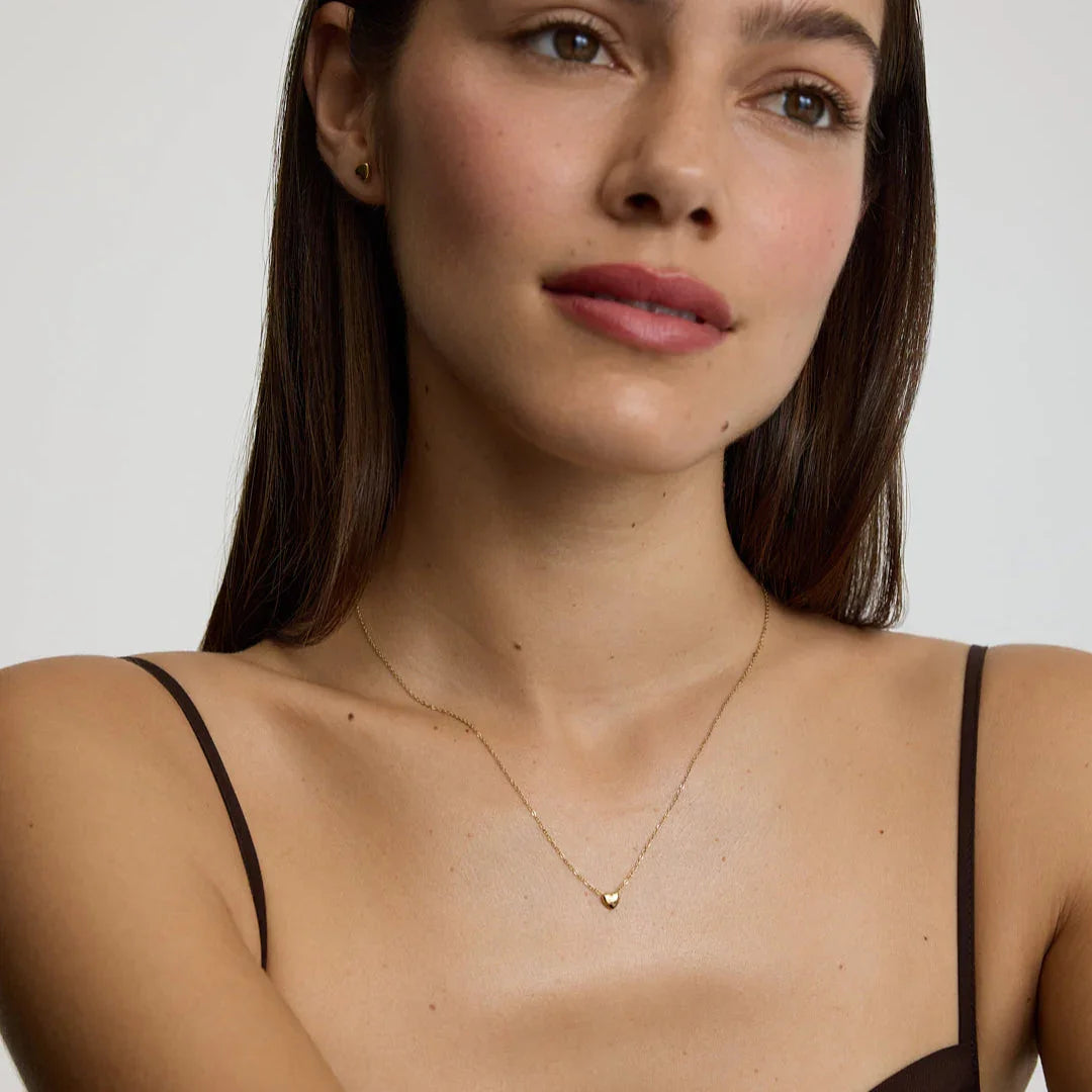 Close-up of woman wearing delicate gold heart pendant necklace with matching heart stud earrings