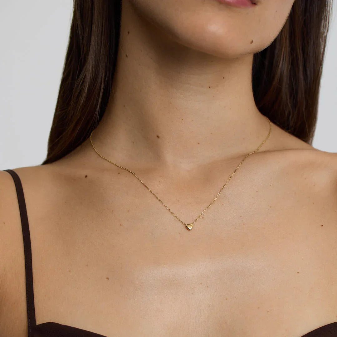 Close-up of woman wearing delicate gold heart necklace with thin chain and dark top