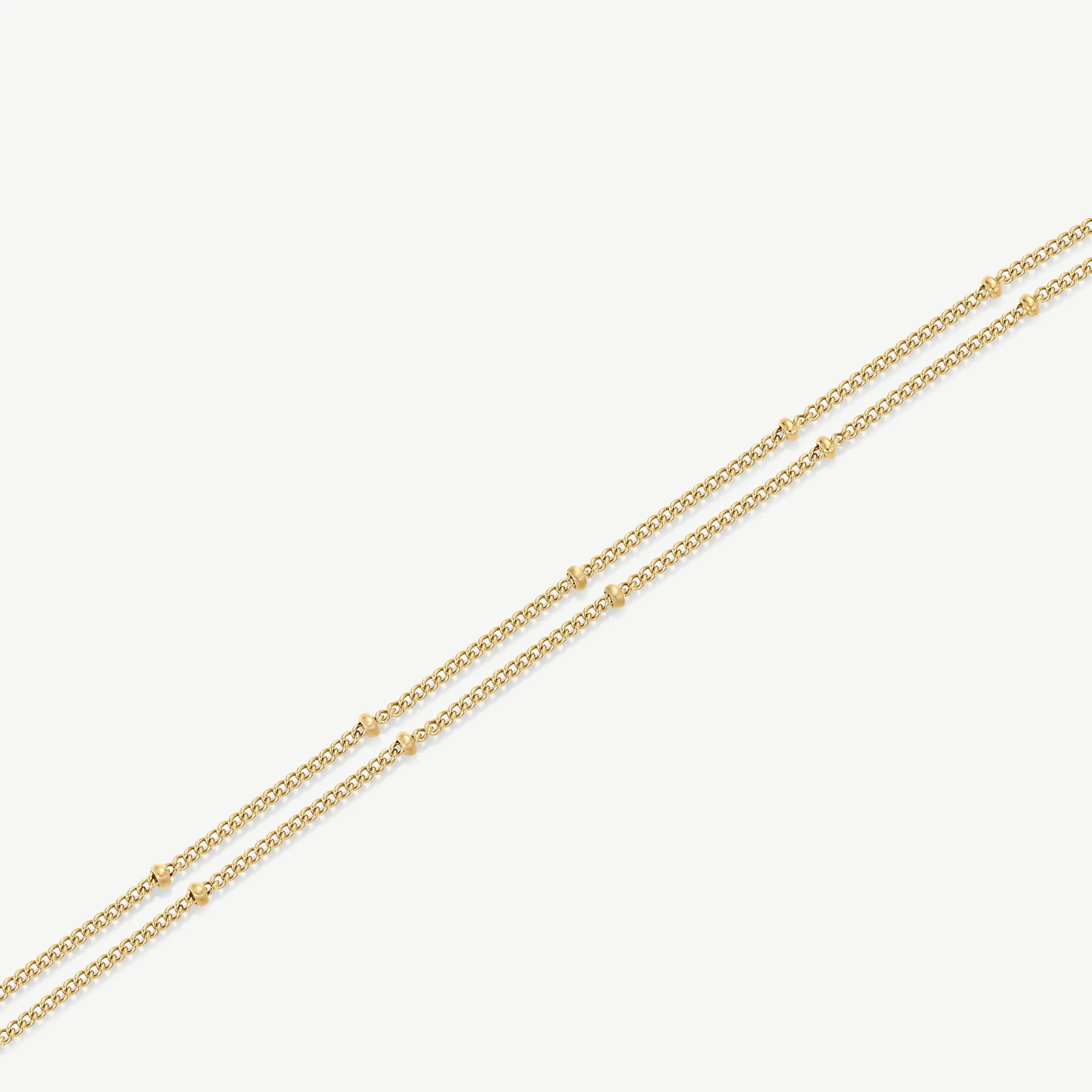 Delicate double-layered gold chain necklace with small gold bead accents on white background
