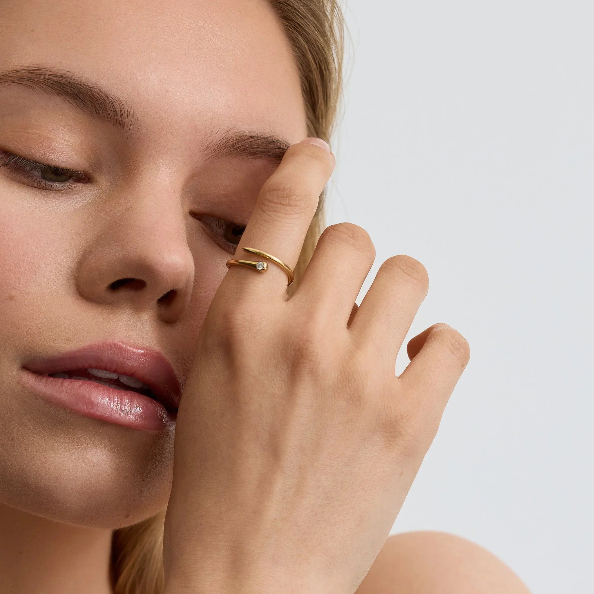 Close-up of woman wearing a gold wave wrap ring with a small diamond on finger