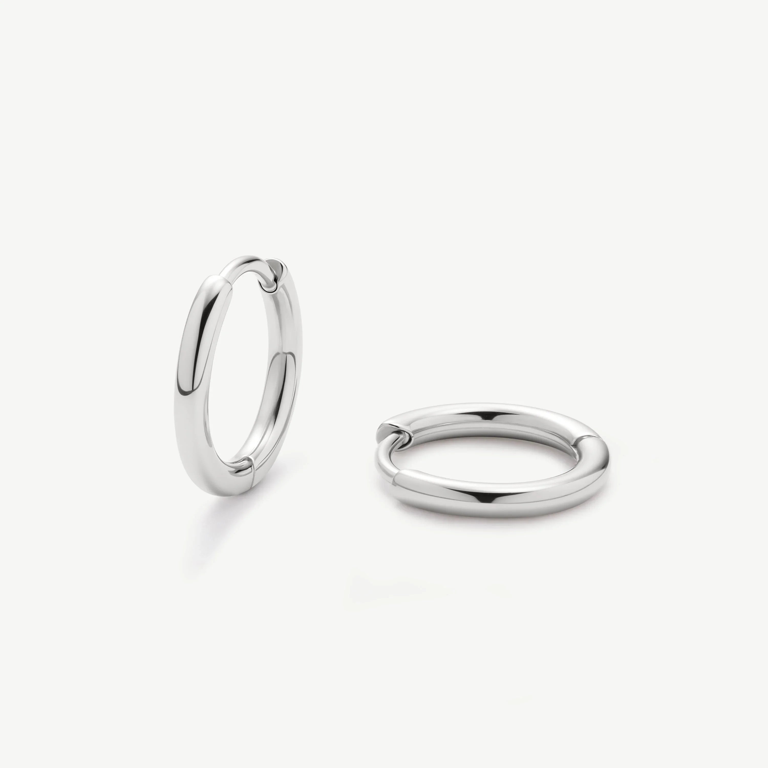 Pair of polished silver hoop earrings on white background, minimalist jewelry design