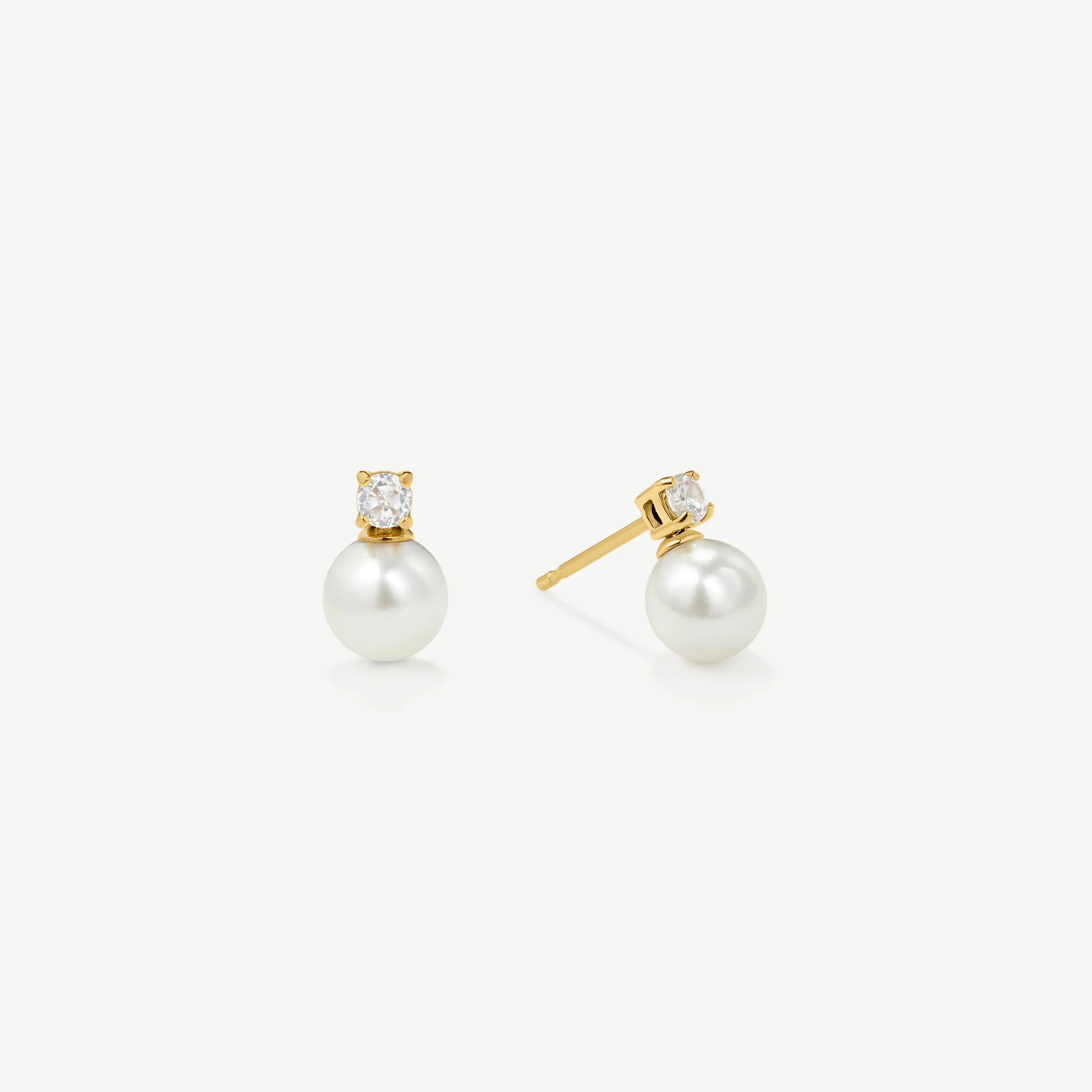 Elegant gold stud earrings with white pearls and small clear gemstones on white background